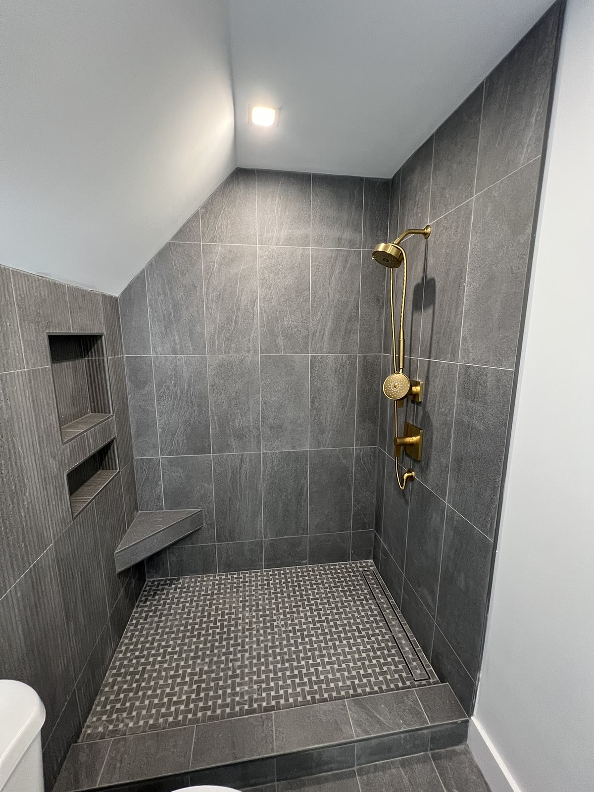 Gray tile walk-in shower with gold fixtures and basketweave mosaic floor