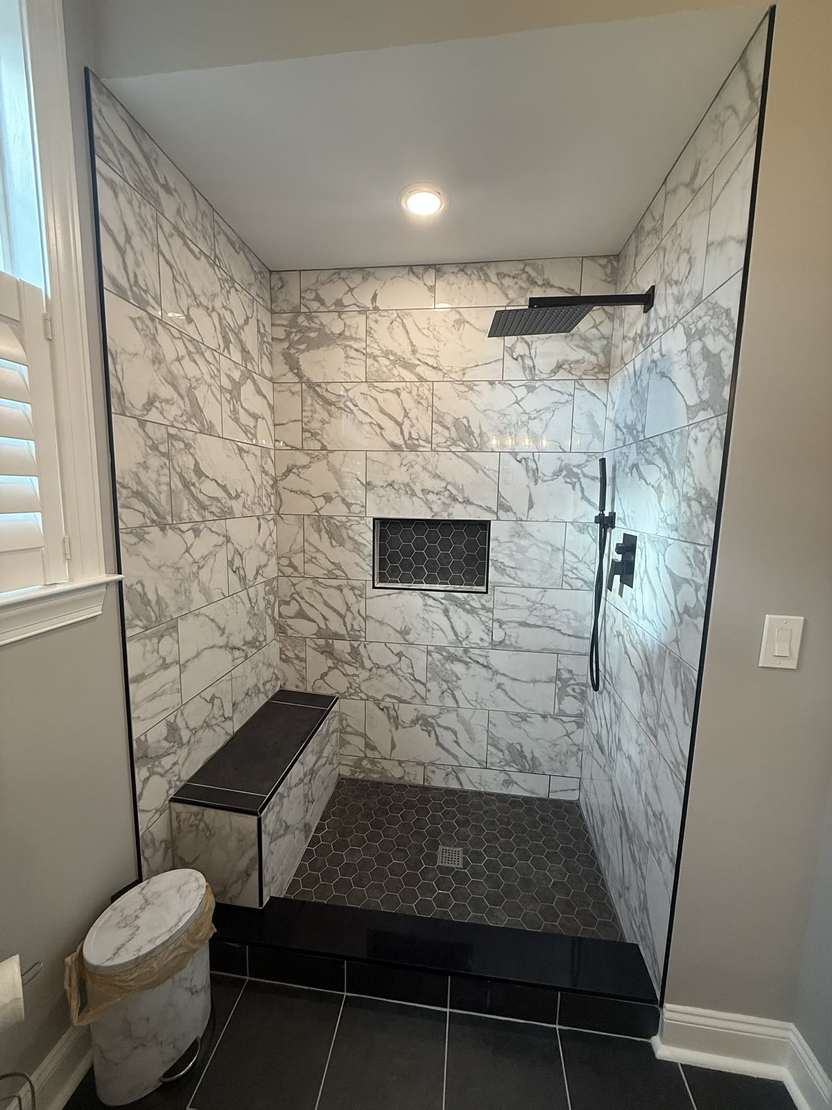 Marble walk-in shower with black hex floor and tile bench, Newtown